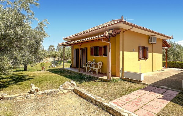 A yellow house with a tiled roof, a porch with chairs, and a small table.