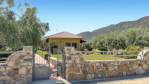 Propiedad de paredes de piedra con un edificio amarillo, una reja y montañas al fondo.
