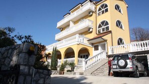 A multi-story yellow building with balconies, a stone wall, and a parked SUV.