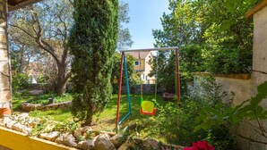A garden with a swing set, a stone wall, and a house in the background.