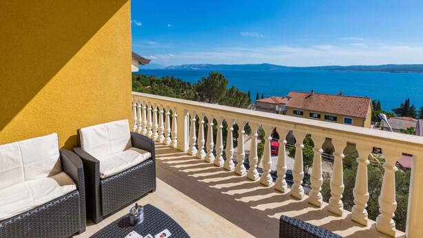 A balcony with wicker furniture, a railing, and a view of the sea and buildings.
