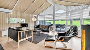 Una sala de estar moderna con televisor, sofá y comedor con asientos exteriores.