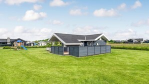 Una casa moderna con un patio trasero amplio, un área de juegos y un espacio exterior techado.