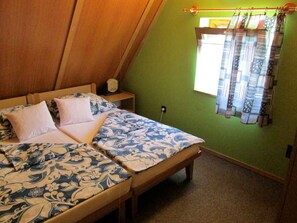 A bedroom with a bed, two pillows, a nightstand, a lamp, and a window with curtains.