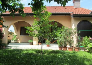 A building with a red-tiled roof, arched doorways, and potted plants in the foreground.