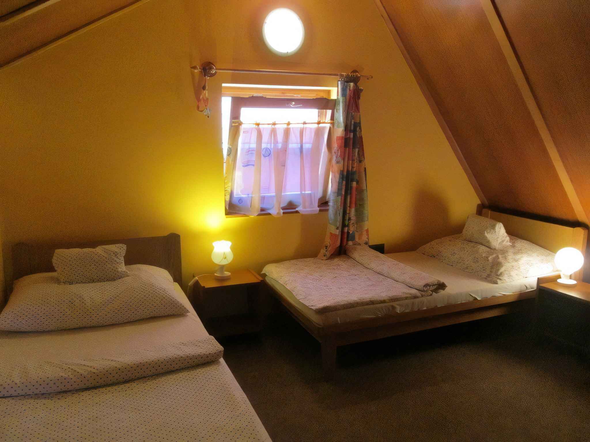 Una habitación de forma triangular con dos camas, una ventana con cortinas y una mesita de noche con lámpara.