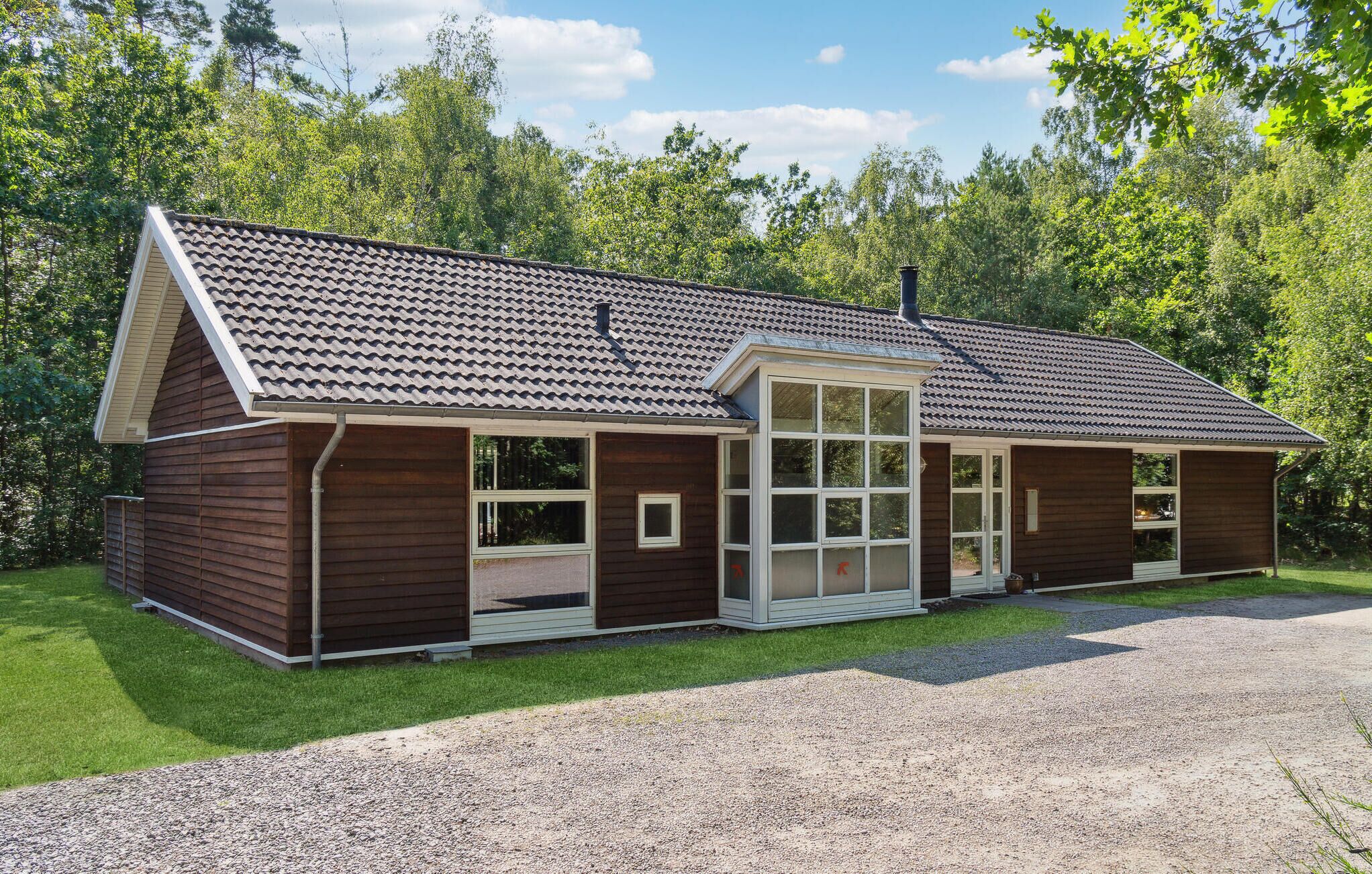A two-story wooden cabin with a sloped roof, large windows, and a gravel driveway.