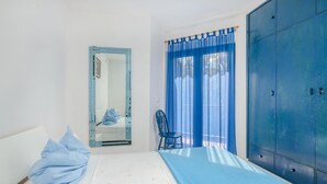 A bedroom with a bed, a chair, a wardrobe, and a window with blue curtains. - Stunning home in Malinska (Malinska)