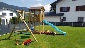 Ein Spielplatz mit Rutsche und Klettergerüsten, umgeben von einem eingezäunten Bereich mit Rasenfläche.
