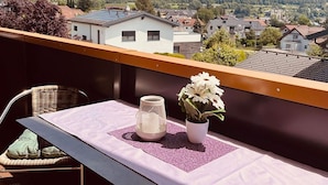 Ein Balkon mit Tisch, einem Stuhl, einer weißen Vase mit Blumen und einer Zierlaterne.
