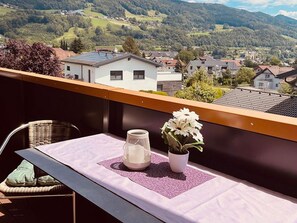 Un balcon avec une table, une chaise, un vase blanc orné de fleurs et une lanterne décorative.