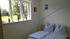 Ein Schlafzimmer mit Bett, einem Fenster mit Pflanzen und einem Wandbild.