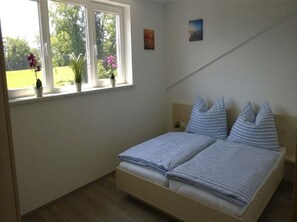 Une chambre à coucher avec un lit, une fenêtre ornée de plantes et un tableau accroché au mur.