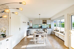 A modern kitchen with white cabinets, a dining area with a wooden table and chairs, and a built-in bench with cushions.