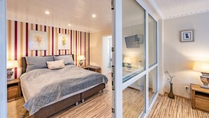 Un dormitorio con cama, mesitas de noche, lámpara, cuadro enmarco, puerta corrediza de vidrio y suelo de madera.