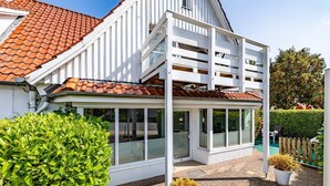 Una casa moderna con techo de tejas rojas, fachada blanca y un porche cubierto con puertas de cristal.
