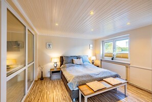 A bedroom with a bed, bedside tables, a window, and a view of greenery outside.