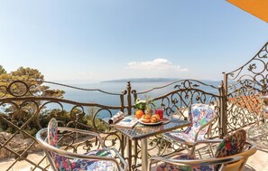 Eine Terrasse mit Metallstühlen und einem Tisch, mit Blick auf eine malerische Seelandschaft und ferne Berge.
