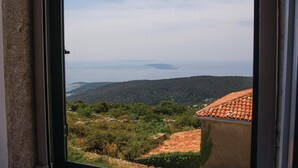 A view from a window overlooking a coastal landscape with terraced fields and a distant body of water.