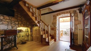 A rustic interior with a stone wall, wooden staircase, and a view to an outdoor patio.