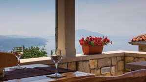 A terrace with a table, two wine glasses, and a potted plant with red flowers.