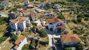 A cluster of traditional stone buildings with red-tiled roofs, surrounded by greenery and stone walls, indicating a historic village setting.