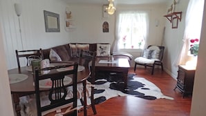 Un salon chaleureux avec un plancher en bois, un tapis en peau de vache, un canapé, une table à manger avec des chaises et une fenêtre avec des rideaux.