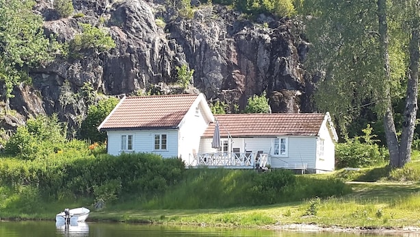 Une maison blanche avec un toit rouge, située au bord d’un lac, avec un bateau amarré à proximité.