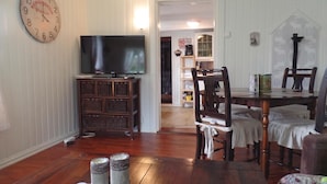 Un salon avec un téléviseur posé sur un meuble en bois, une table à manger avec des chaises et une horloge au mur.