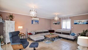 Ein Wohnzimmer mit Ecksofa, blauem Sessel, Couchtisch und einer Deckenleuchte.