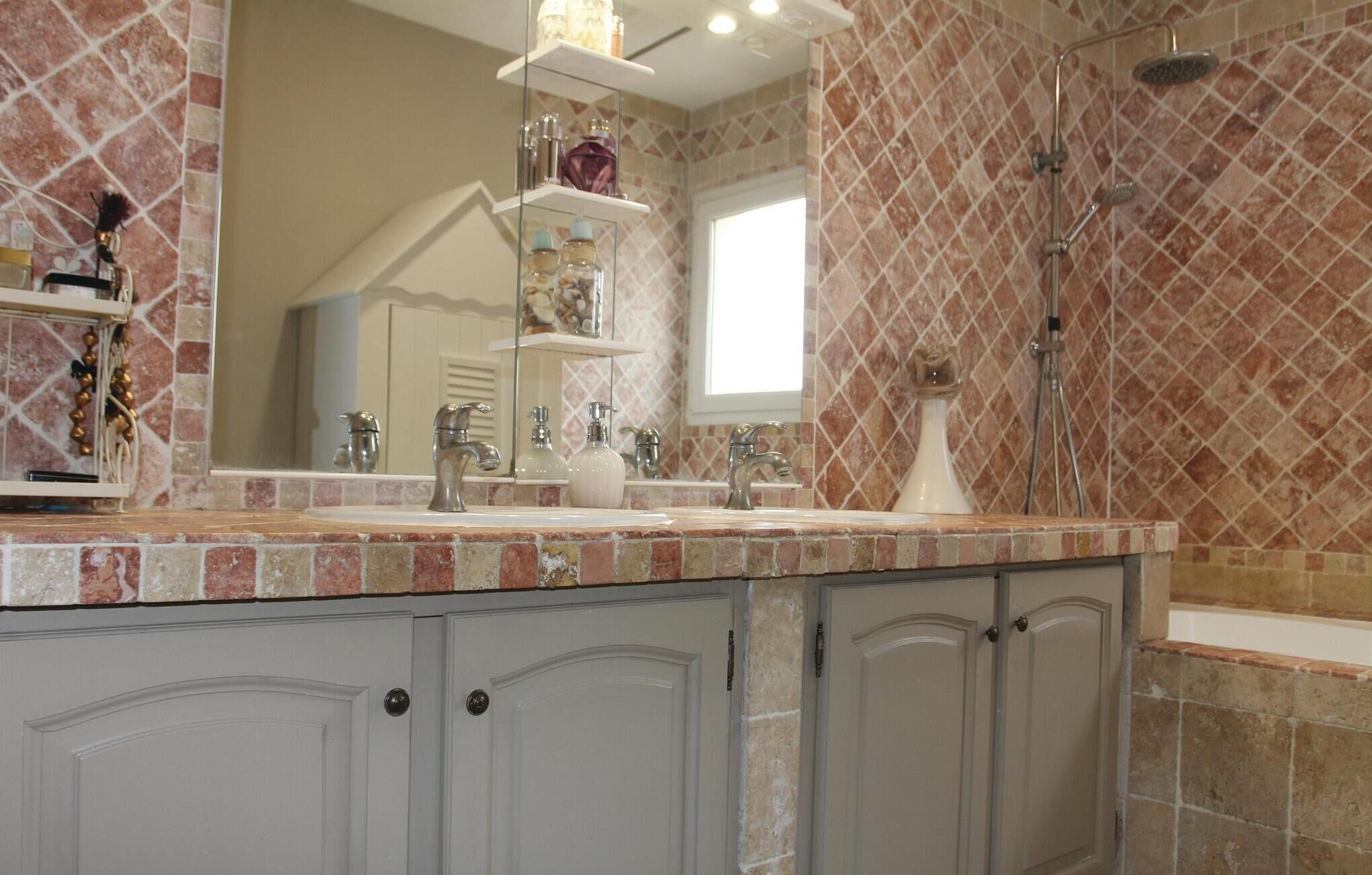 Une salle de bain dotée d’un grand miroir, de deux lavabos, d’une douche et d’un meuble-lavabo avec des placards.