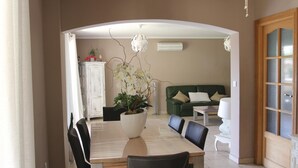 Ein Essbereich mit Tisch und Stühlen, einer Topfpflanze, einem grünen Sofa und einem weißen Schrank.