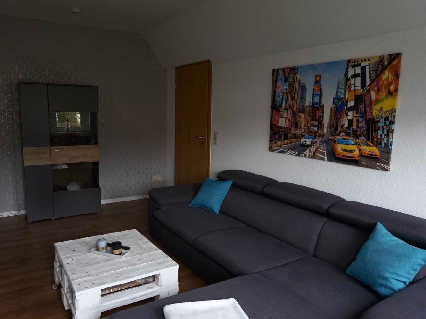 Ein modernes Wohnzimmer mit einem dunkelgrauen Ecksofa, einem weißen Couchtisch und einem Stadtbild an der Wand.