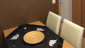 Un comedor con una mesa dispuesta para dos personas, una radio en la pared y una puerta que da a otra habitación.