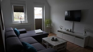 Una sala de estar moderna con un sofá gris, una mesa de centro de madera y un televisor montado en la pared.