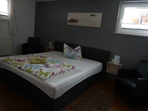 Quarto com cama, mesa de cabeceira, cadeira, janela e uma obra de arte na parede.