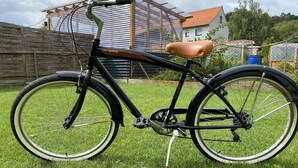 Una bicicleta estática con asiento marrón, estructura negra y neumáticos blancos, estacionada sobre un césped.