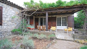 Ein Steinhaus mit überdachter Terrasse, Holzmöbeln und einem Garten.