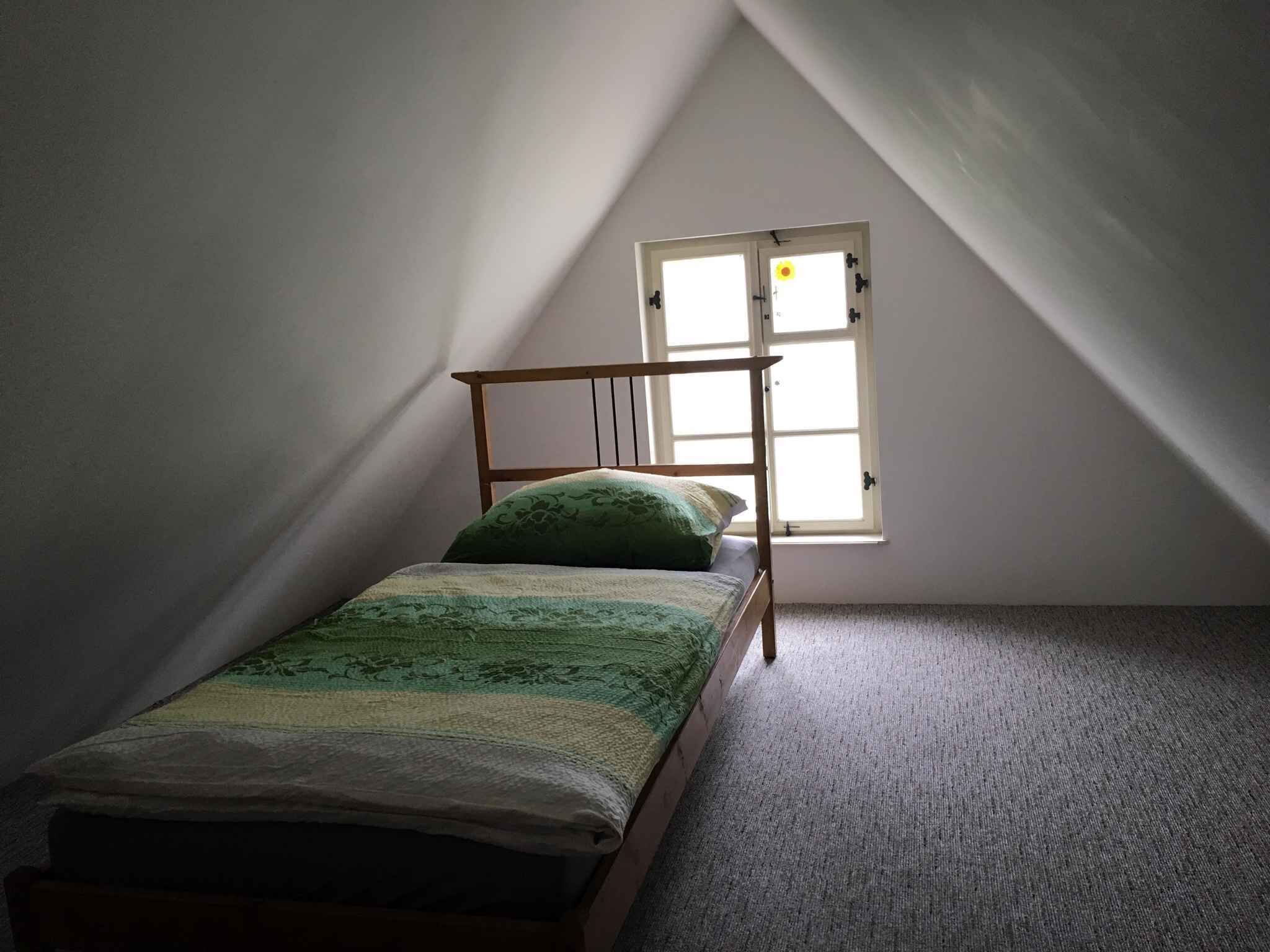 Een kleine kamer met een enkel bed, schuine plafond en een raam.
