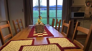 A dining table with floral placemats and a centerpiece, set in a room with a view of a green field through large windows. - Holiday home with large terrace and Wifi in beautiful surroundings (Bozanov)