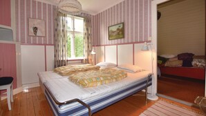 Un dormitorio con cama, ventana con cortinas, lámpara de noche y un cuadro en la pared.