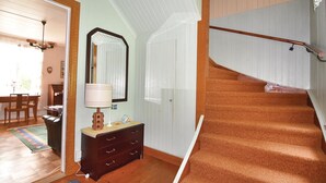 Una escalera con barandilla de madera y peldaños alfombrados, un aparador de madera con cajones, un espejo y una ventana con persianas.