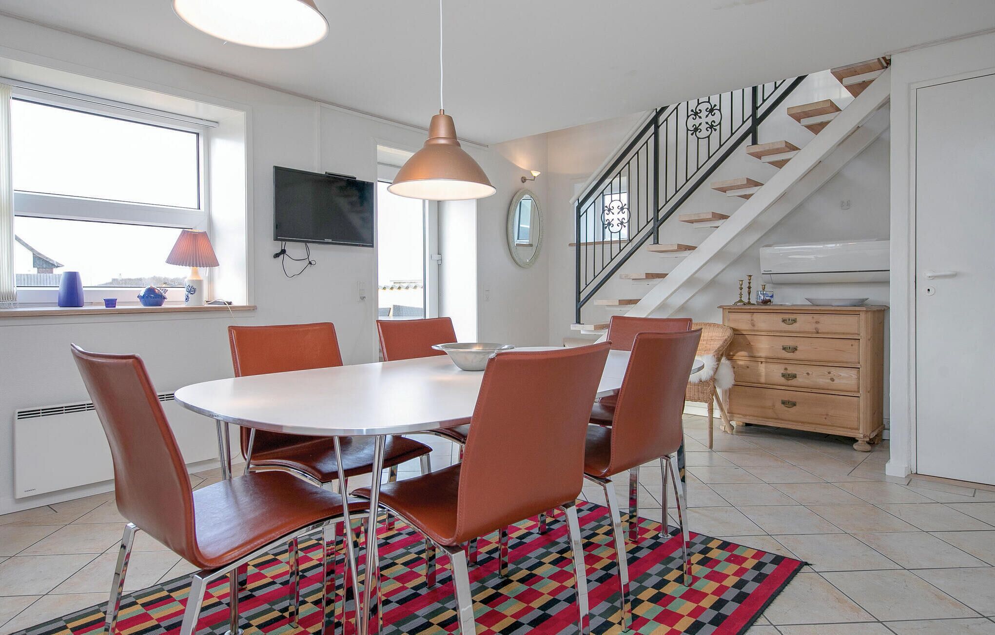 A modern kitchen with a dining table, chairs, and a colorful rug.