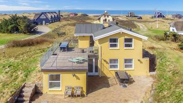 Une maison jaune à deux étages, dotée d’une terrasse, d’un petit jardin et offrant une vue sur la mer.