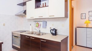 A modern kitchen with a double sink, an oven, and a stove. There are cabinets above the counter and a small shelf with decorative items.