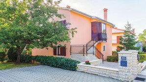 A residential building with a pink facade, a stone entrance, and a staircase leading to a balcony.