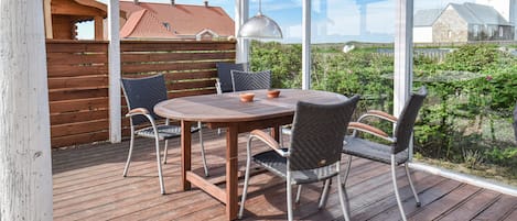 An outdoor patio with a wooden table and chairs, a pergola, and a view of a church and greenery.