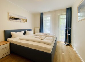 A bedroom with a bed, a nightstand, a radiator, a window with curtains, and a painting on the wall.