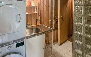 Une cuisine de taille réduite, équipée d’un lave-linge, d’un évier et de meubles de rangement en bois.