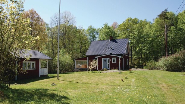 Una casa vermella amb un teulat negre, una casa blanca més petita i un jardí amb gespa i arbres.